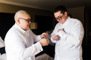 Best man helps groom with cuff links in hotel room