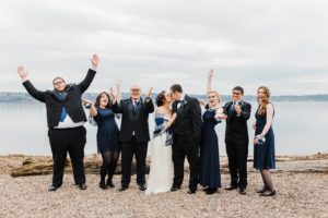 full bridal party cheers as bride and groom share a kiss