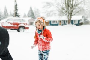 four year old in red coat laughing in the snow
