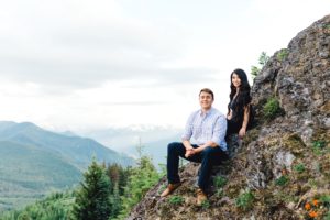 Couple sits a couple feet a part looking into camera on mountain side