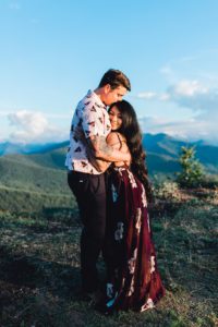 Man kisses woman's head over looking mountains against a blue sky