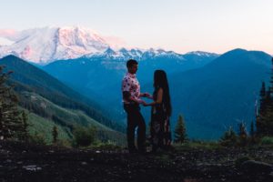 Couple holds hands in darkness overlooking Mt. Rainier glowing at sunset.